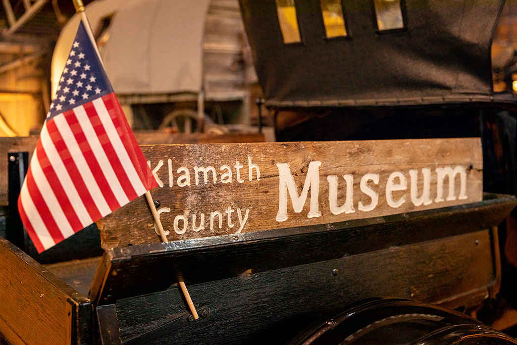 American Flag on a wagon with a wooden sign that reads 'Klamath County Museum'.