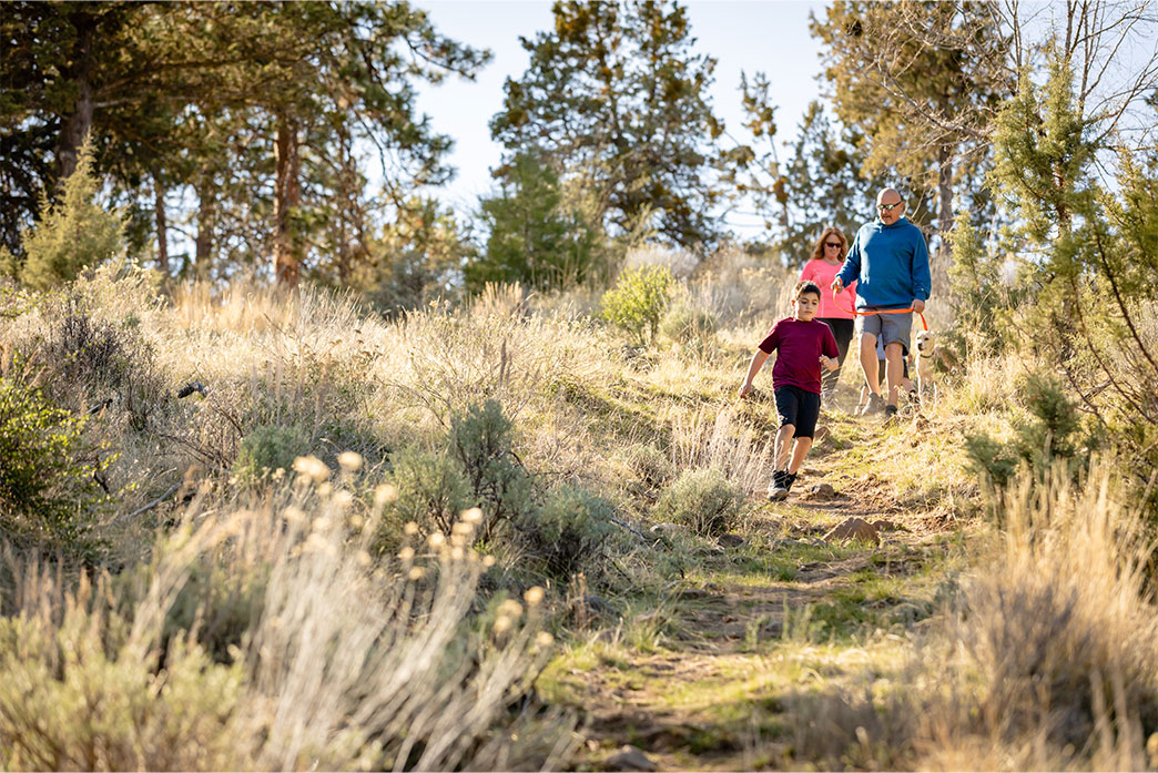 Family of three hiking down a slope with sage and dry grass.